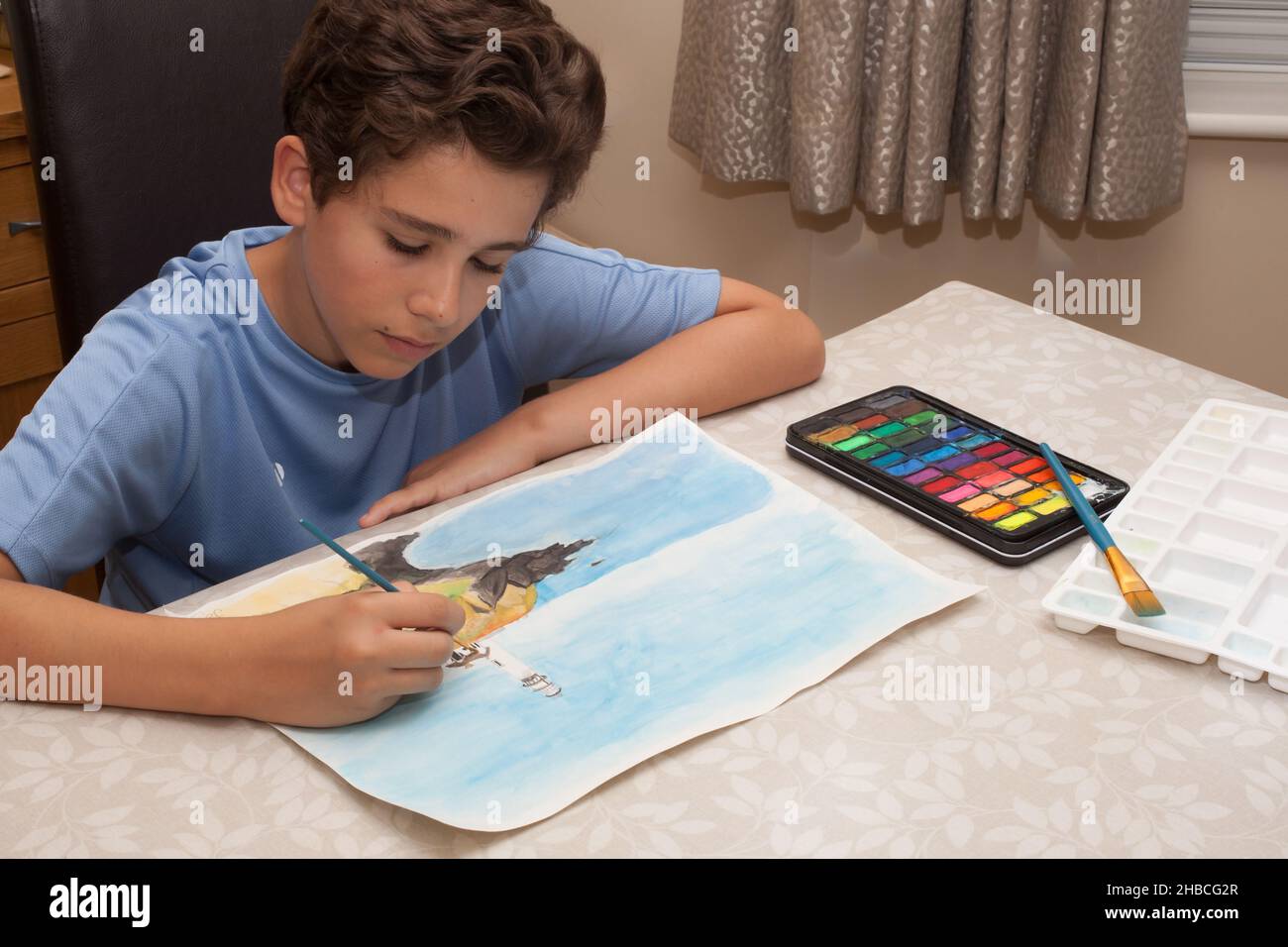 A boy painting a watercolour picture of a coastline, taken on the 13th of August 2020 in Wool, Dorset, UK Stock Photo