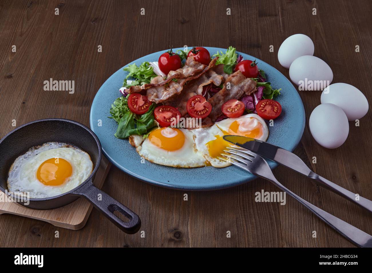 Fried eggs with bacon, lettuce and cherry tomatoes on a blue plate Stock Photo