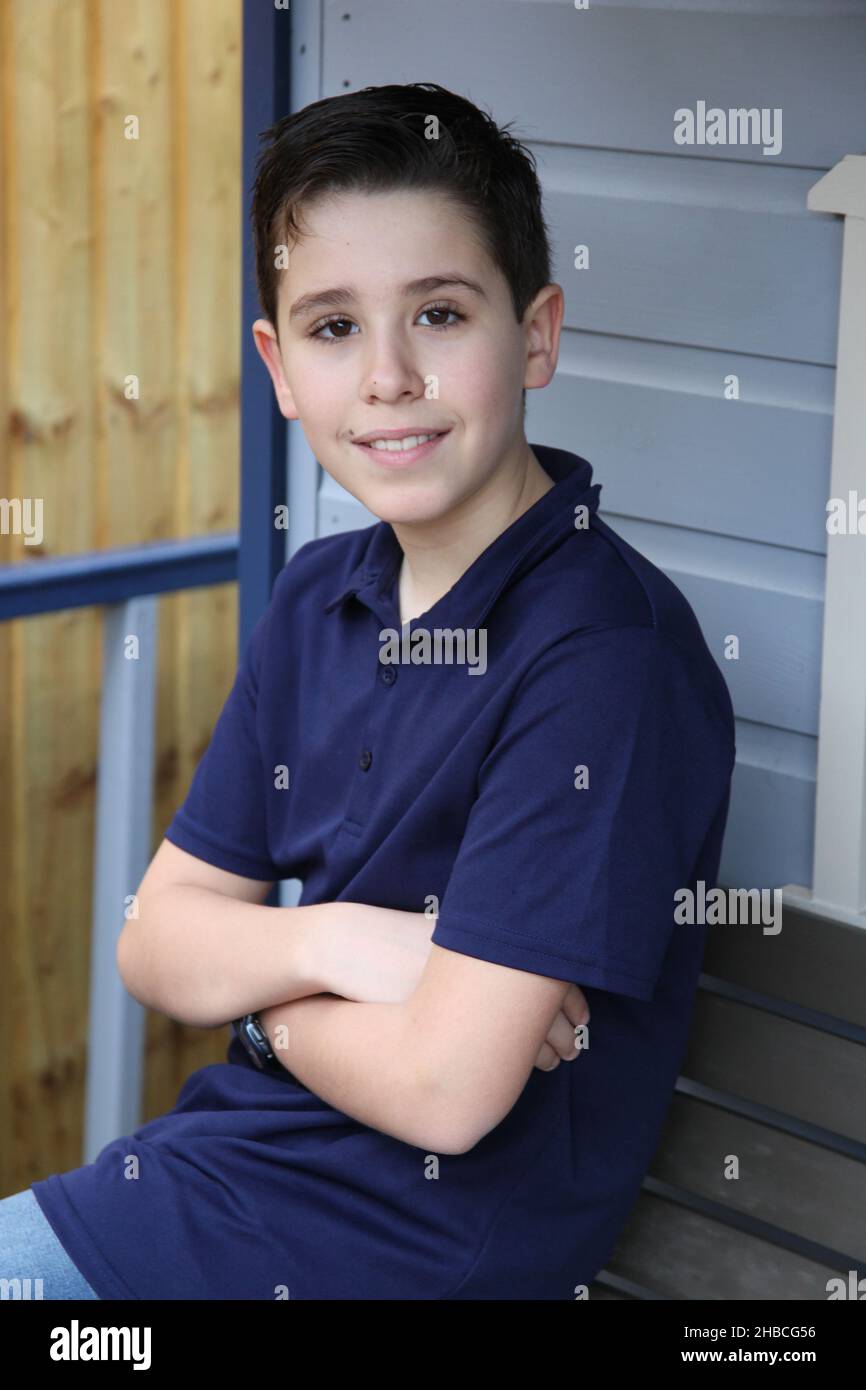 A portrait of a twelve year old boy with his arms folded lit by ambient light Stock Photo