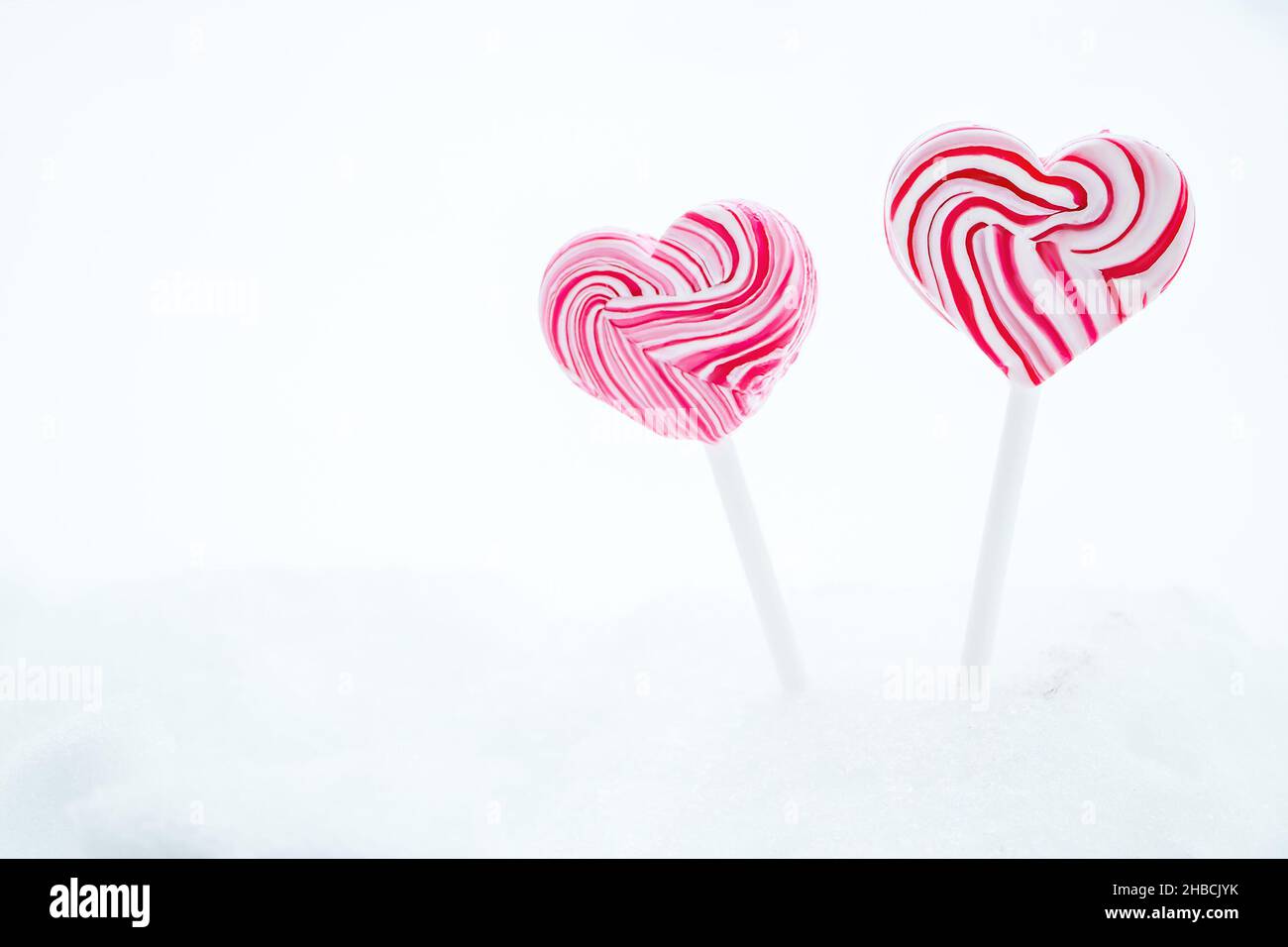 Two pink heart-shaped lollipop. Caramel candy on a stick on white background. Sweet gift for valentines day. Copy space Stock Photo