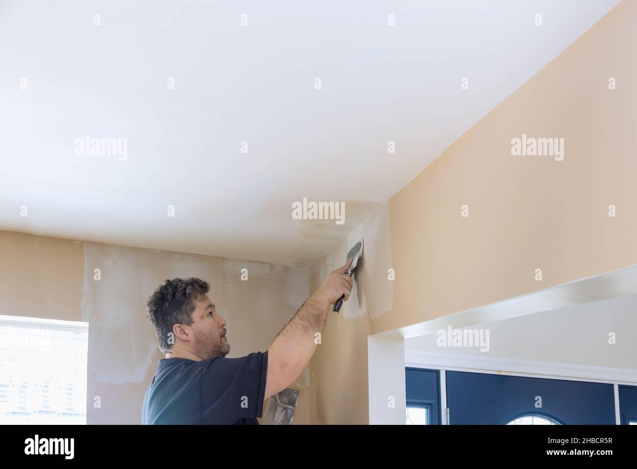 Man putting up a plasterboard a spatula on the white plaster on the wall. Stock Photo