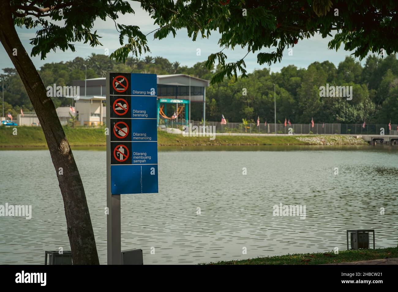 No swimming, no fishing, don't litter and no diving signboard near the lake written in Malaysian language. Stock Photo