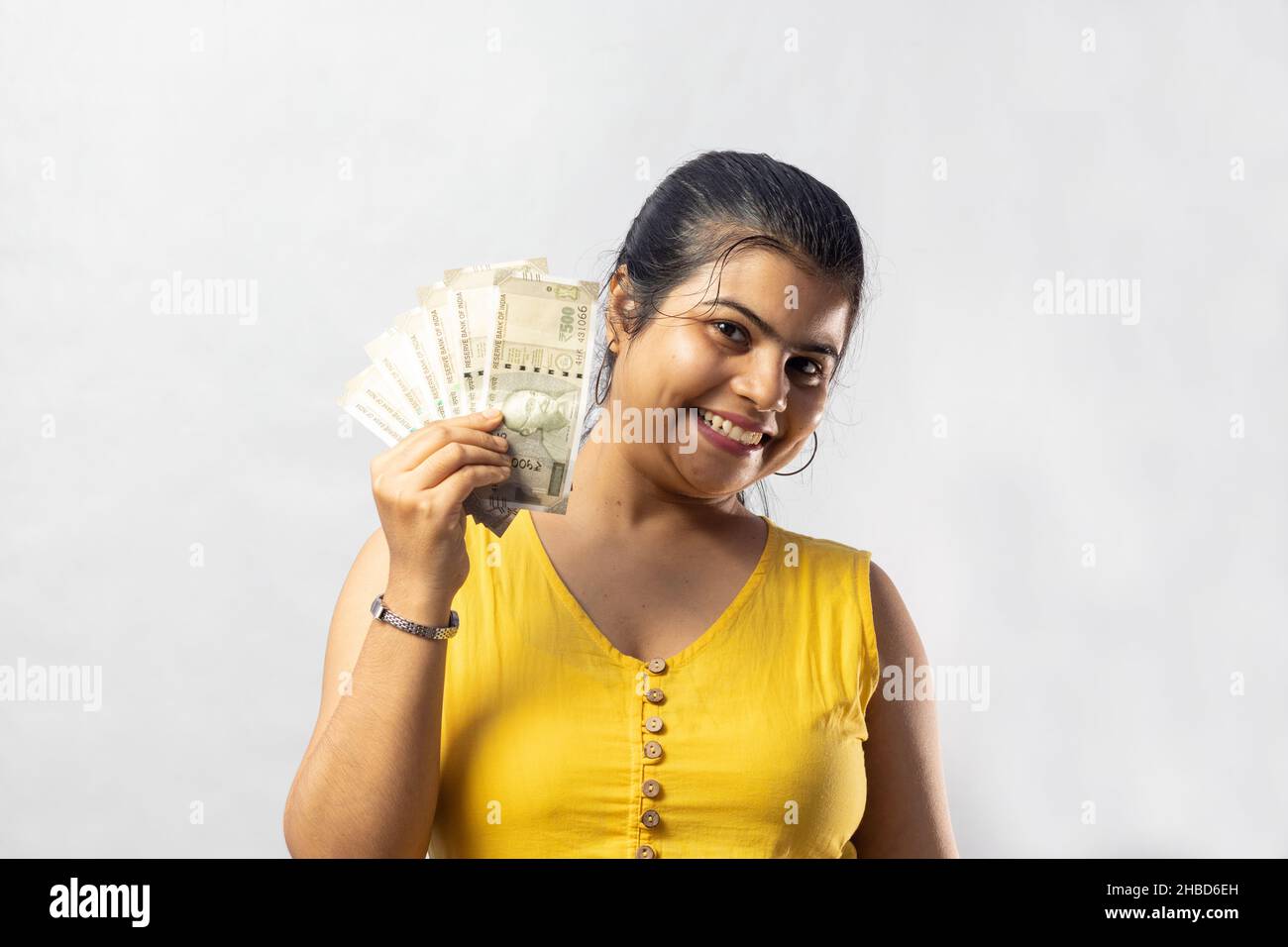 A beautiful Indian woman in yellow dress with cash smiling at the camera on white background Stock Photo