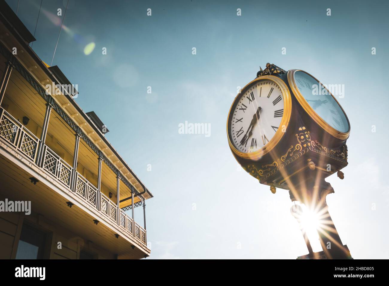 Old golden vintage clock with greek numbers, sunflare, building and blue sky in the background. Old town in Tbilisi. Georgia. 2020 Stock Photo