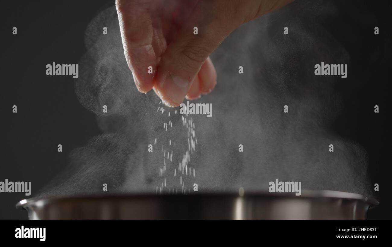 man adding salt to boiling water in saucepan with strong backlight