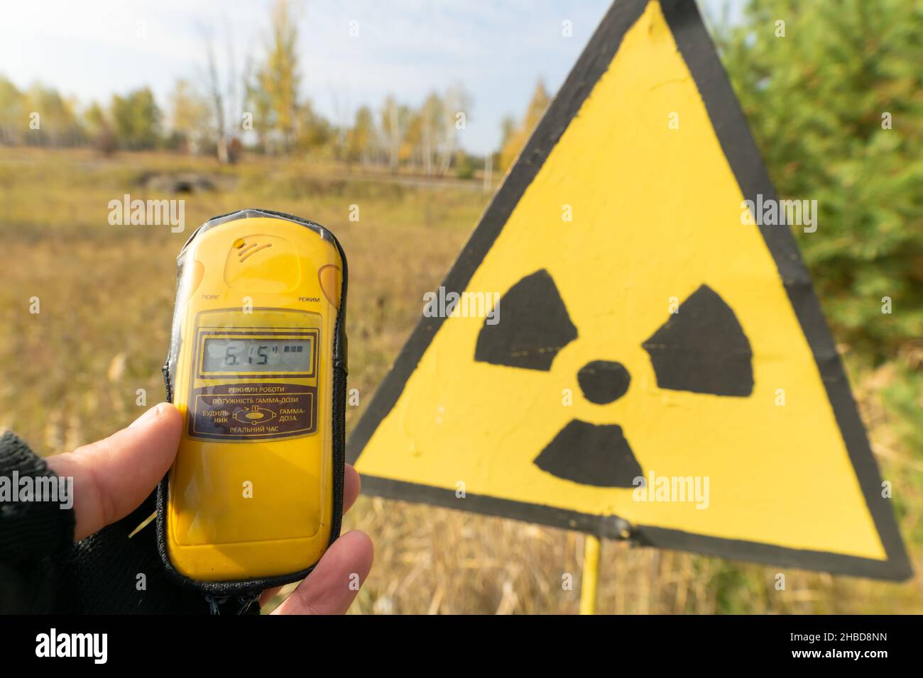 Yellowgeiger counter on the hands shows radiation level near radiation symbol in front of red forest in autumn.Ukraine. Chernobyl group tour. Stock Photo