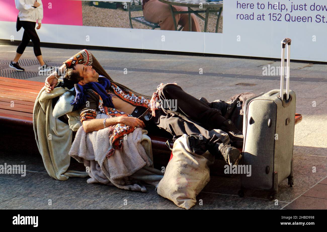 Traveller with bags and luggage resting comfortably on a city bench in