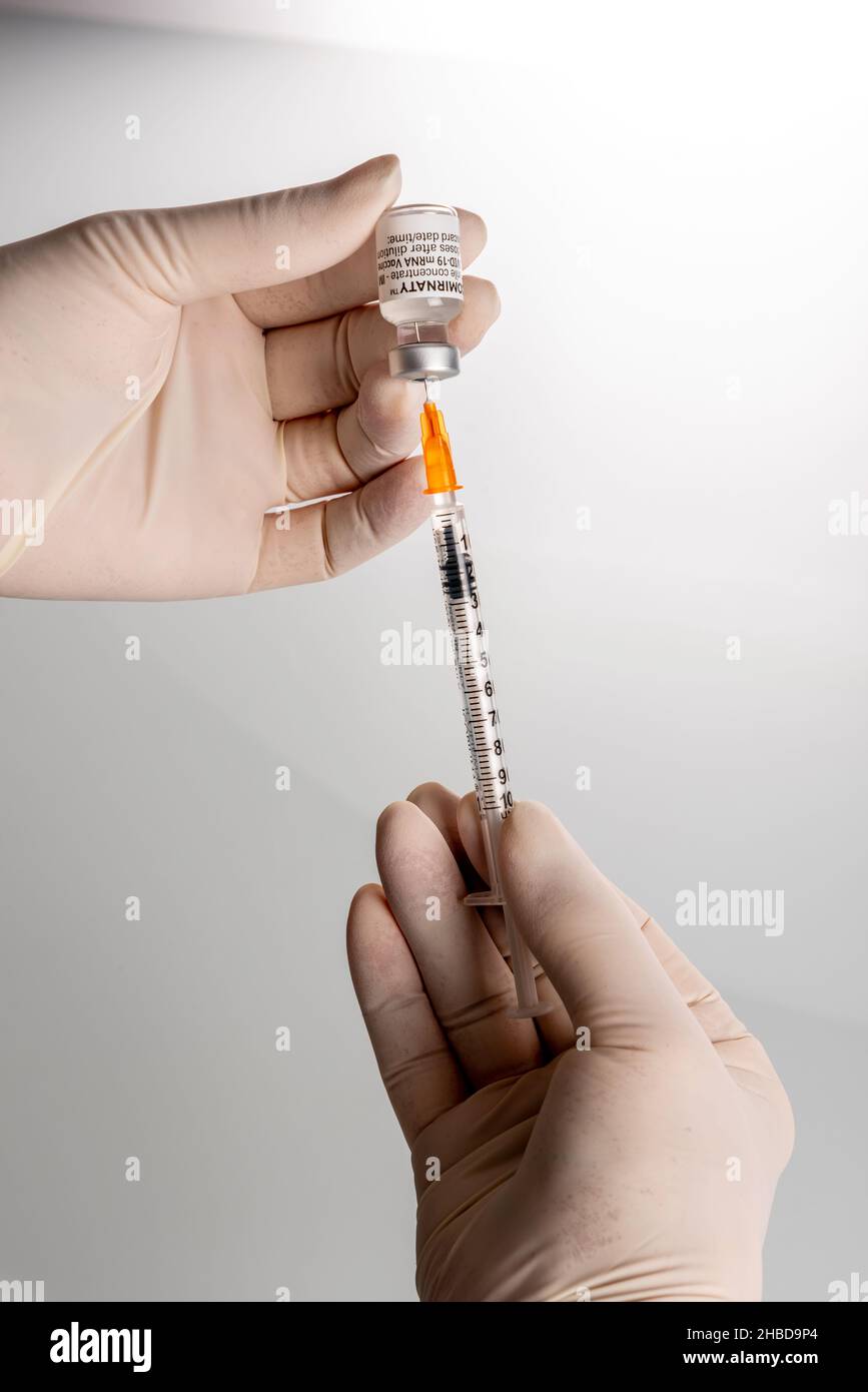 Turin, Italy - December 18, 2021: Pfizer-BioNTech COVID-19 Vaccine Comirnaty vials, nurse hands with latex glove aspirating a dose of vaccine Stock Photo