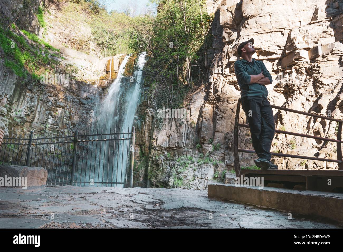 Male tourist standing relaxed in front of Tbilisi waterfall and spring nature. Travel destination - Georgia. 2020 Stock Photo