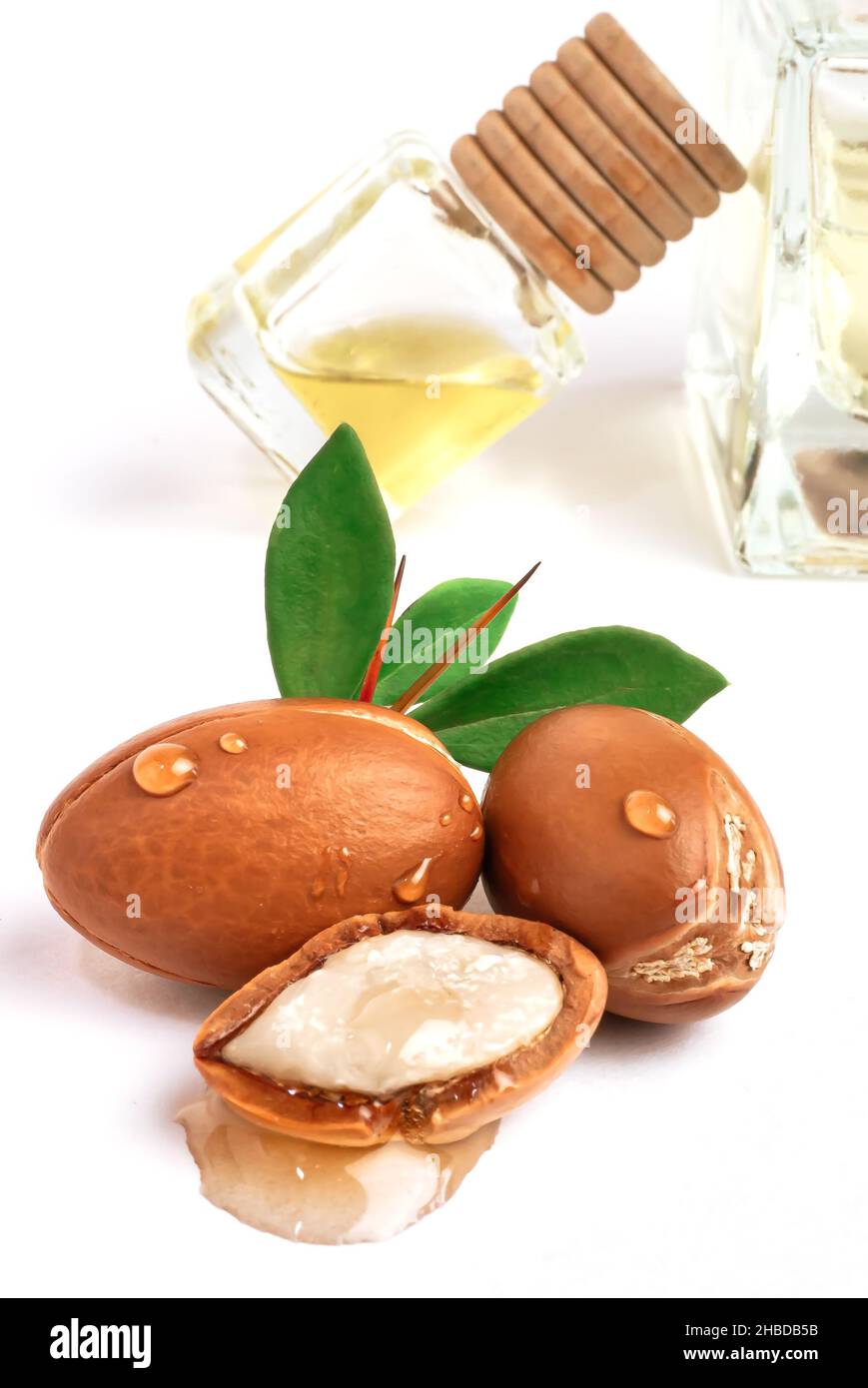 Three argan nuts with green leaves glass bottles on isolated white