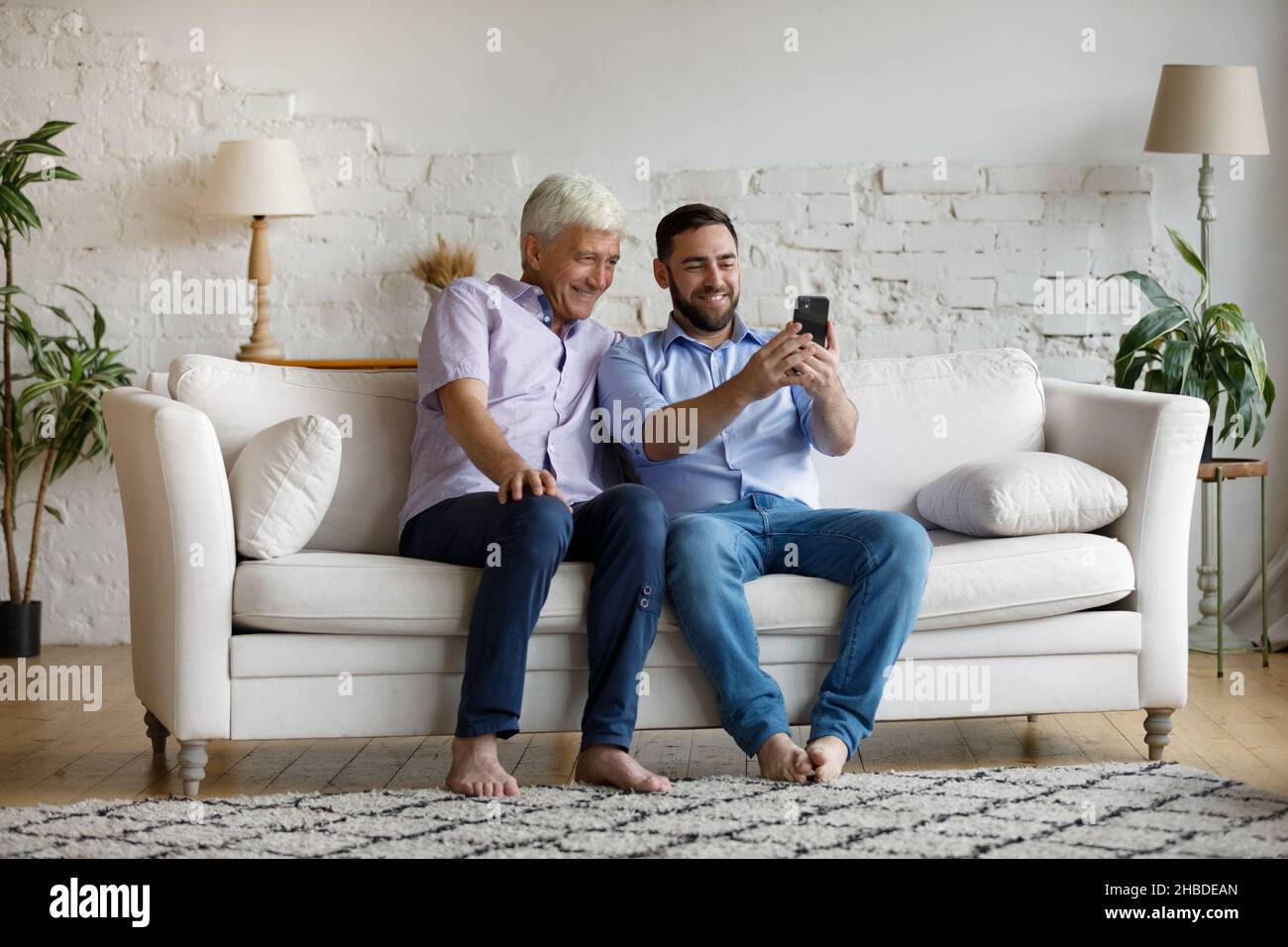 Happy young man using cellphone with older father. Stock Photo