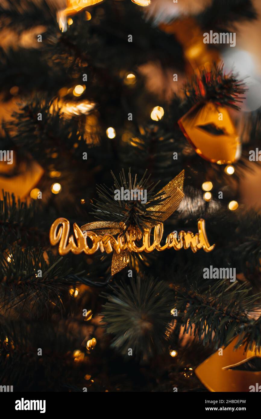 Golden Christmas decoration with text WONDERLAND hanging on the Christmas tree. Golden bokeh garland lights on festive winter background Stock Photo