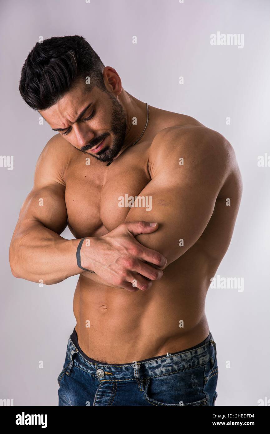 Muscular man holding his elbow with one hand and grimacing in pain Stock Photo