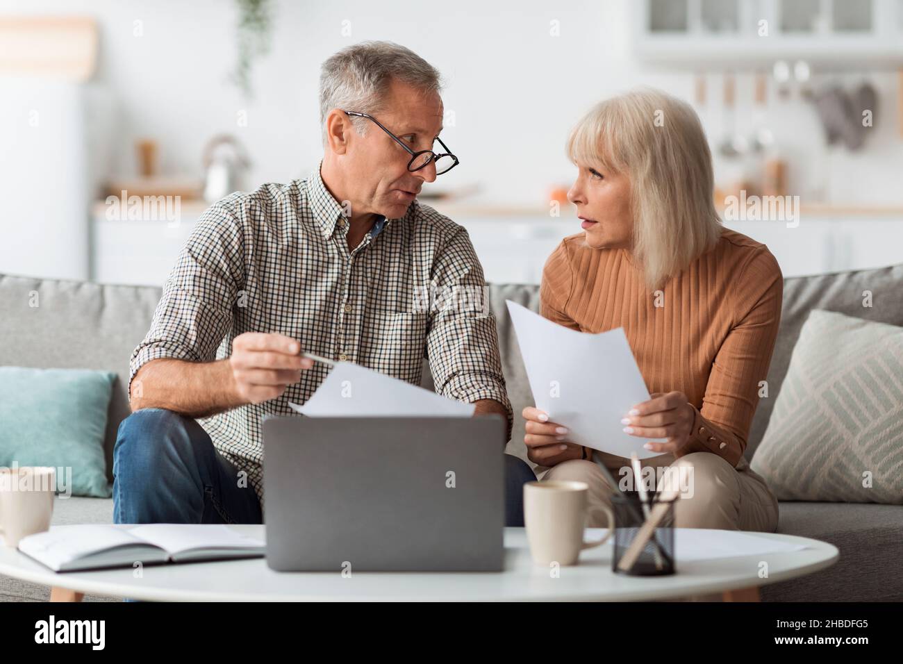 Senior Couple Holding Papers Reading Documents Sitting At Laptop Indoor Stock Photo