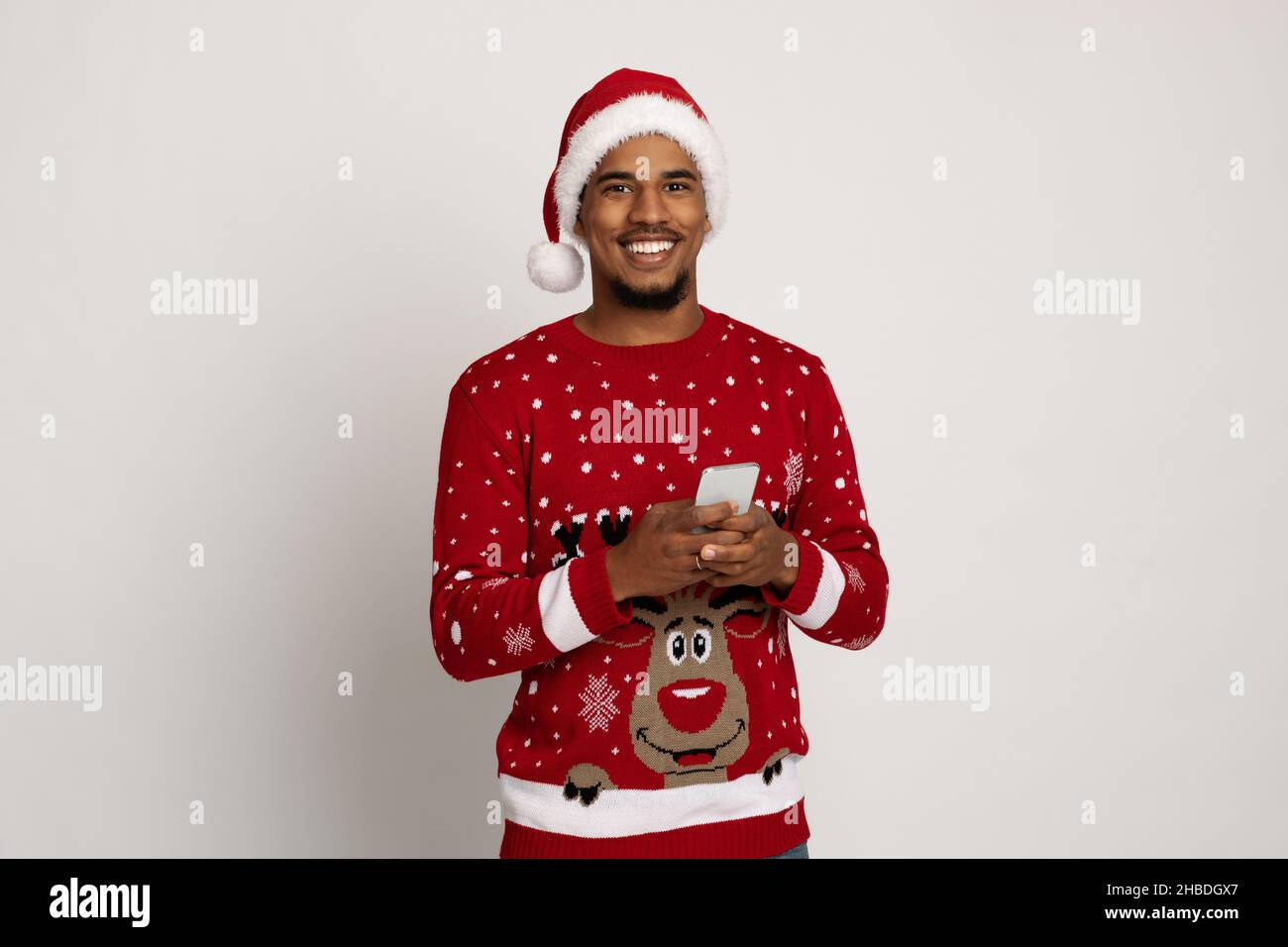 Cheerful black guy in Santa hat using smartphone Stock Photo