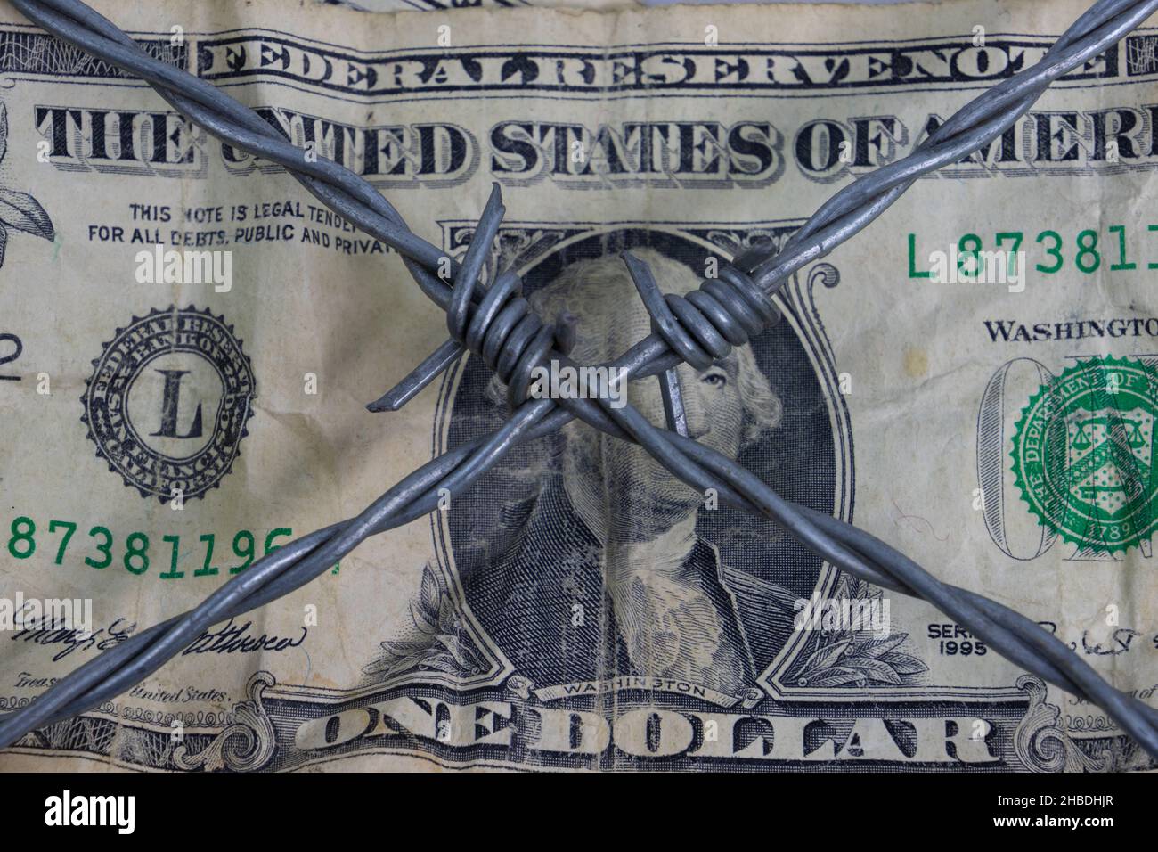 Close up of wrinkled dollar bill with barbed wire forming an x in the center Stock Photo