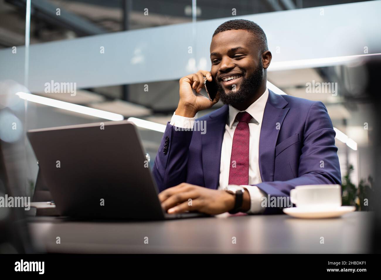 Smiling black manager working on laptop and talking on phone Stock Photo