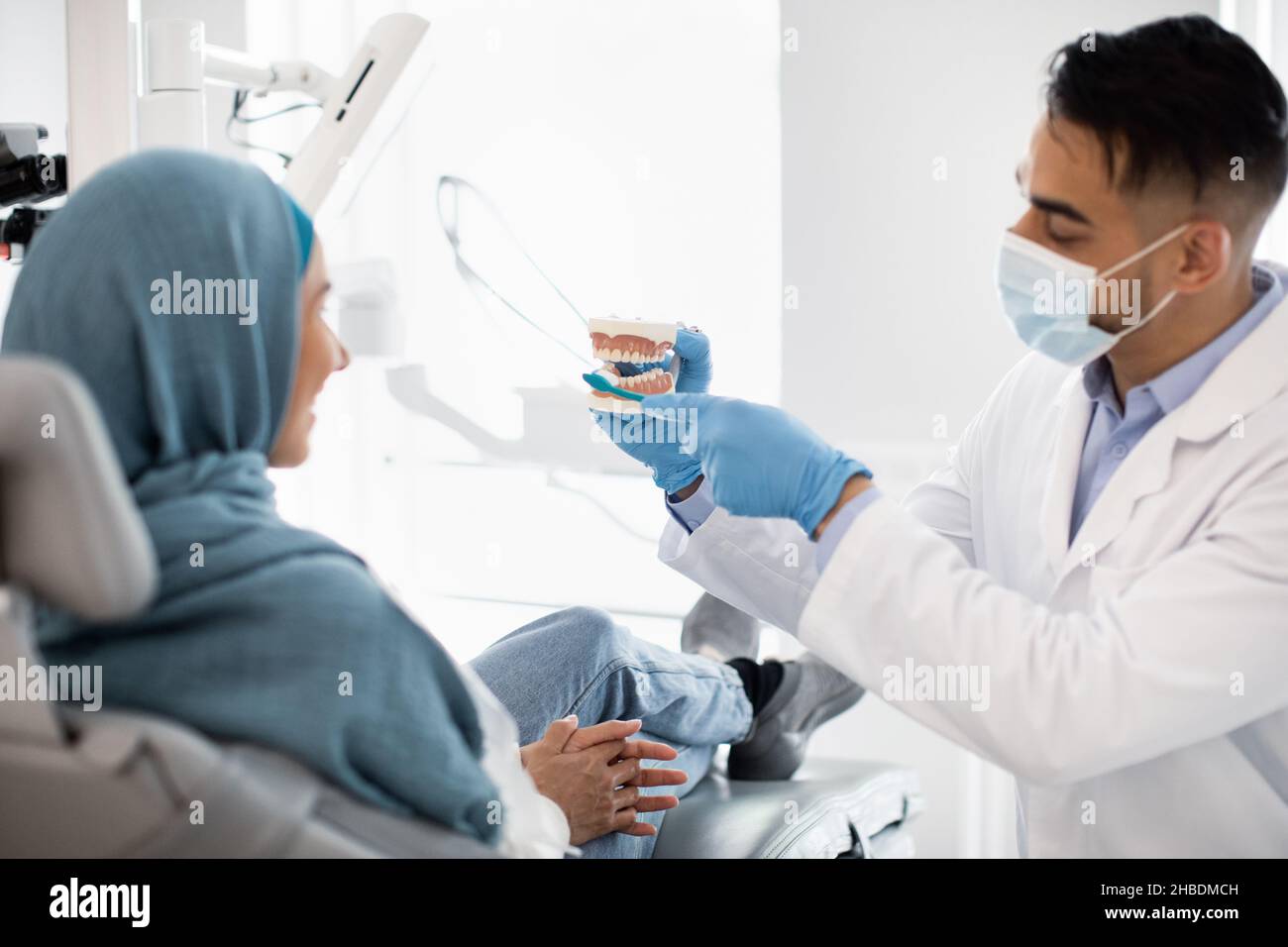 Arab Stomatologist Holding Jaw Model, Teaching Oral Hygiene To Muslim Female Patient Stock Photo