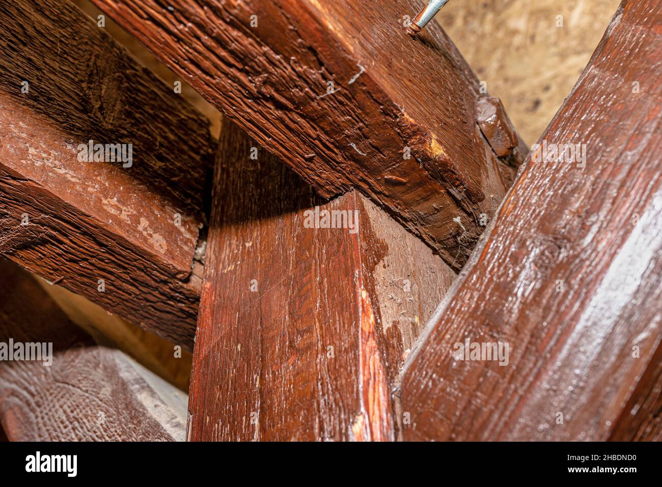 Roof truss visible in the attic house, painted brown with visible cracks in the wood, walls covered with OSB boards. Stock Photo