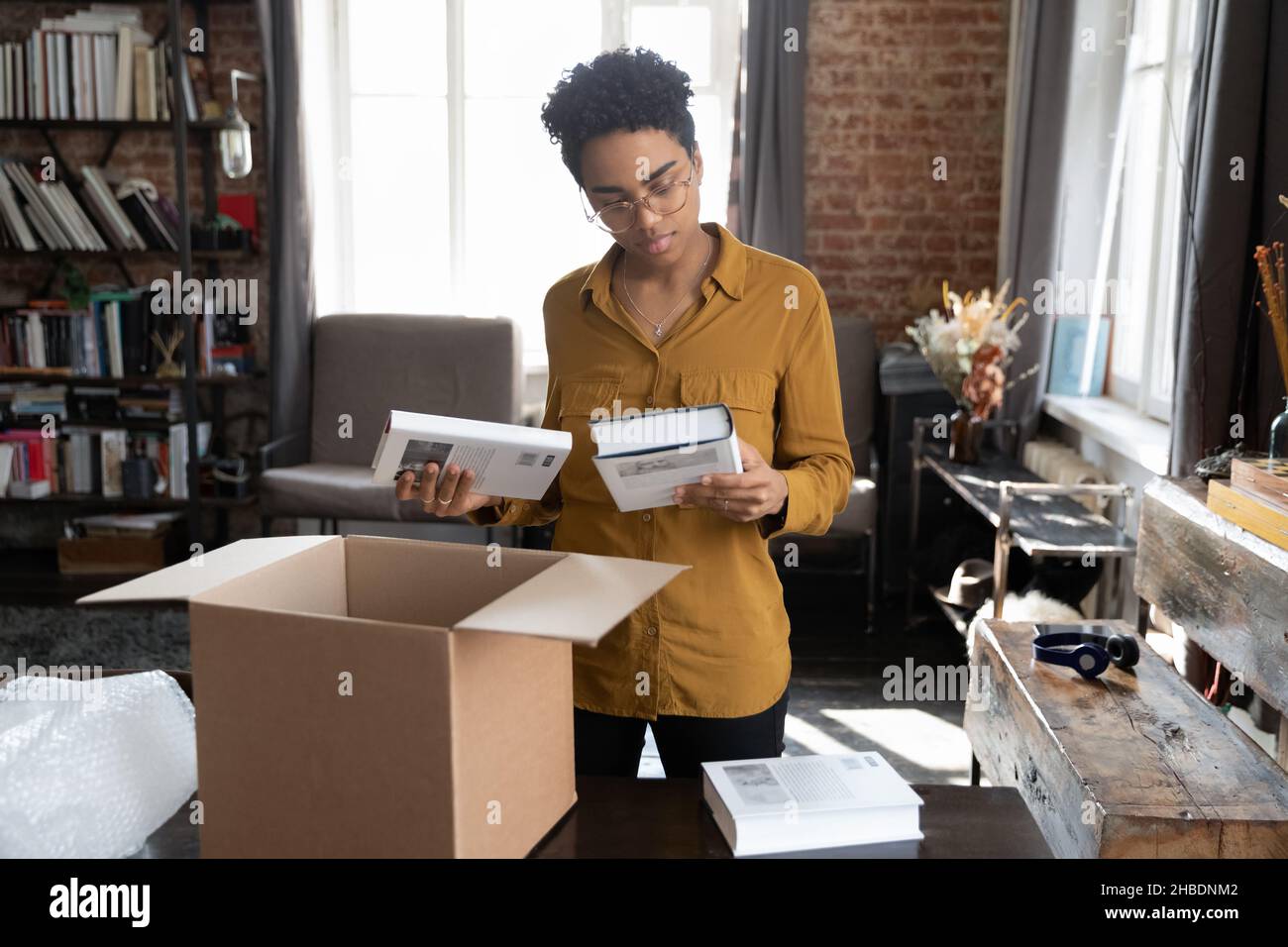 Happy young African American woman unpacking books from box. Stock Photo