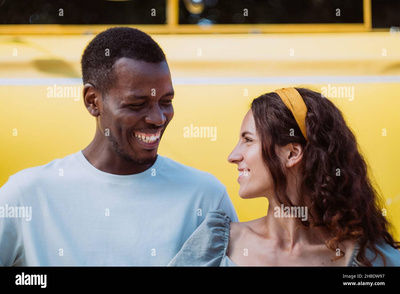 Young Afro-American man and white brunette woman walk and look at each other smiling with love in sunny summer in city park closeup Stock Photo