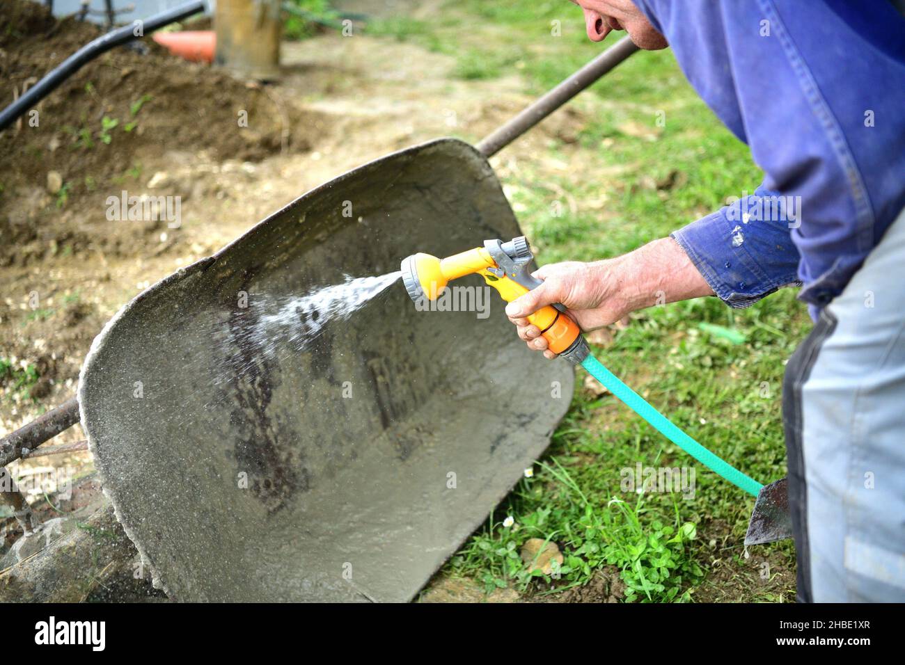 The mason cleaning the wheelbarrow from the mortar with water from a hose after work Stock Photo