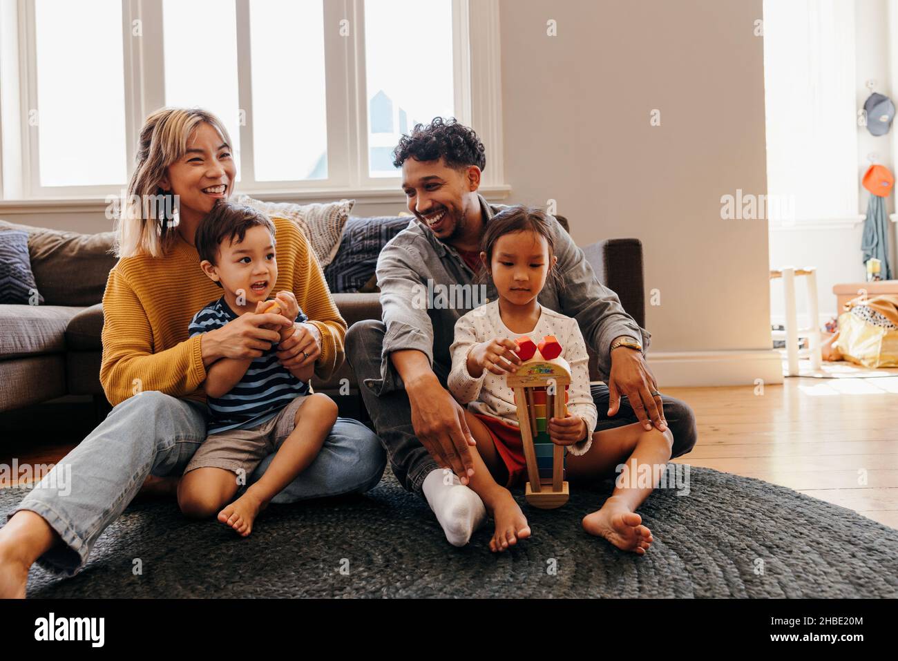 Two young parents playing with their son and daughter in the living room. Mom and dad having fun with their kids during playtime. Family of four spend Stock Photo