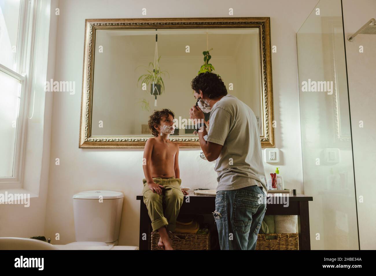 Father showing his son how to shave using shaving cream. Loving father teaching his son his shaving skills in the bathroom. Father and son spending so Stock Photo