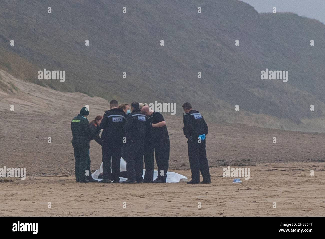 police and ambulance staff stood around a dead body washed up on a