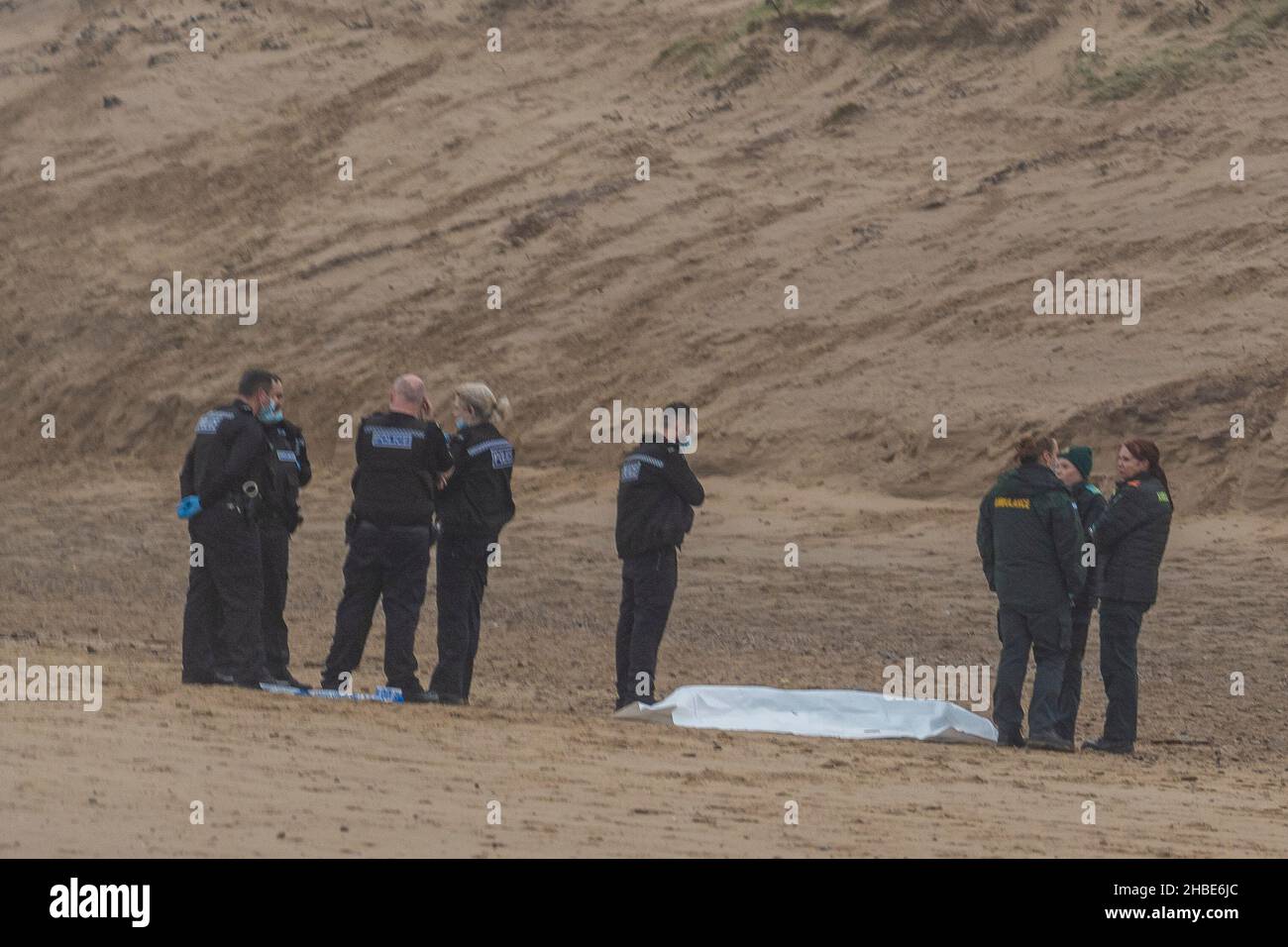police and ambulance staff stood around a dead body washed up on a