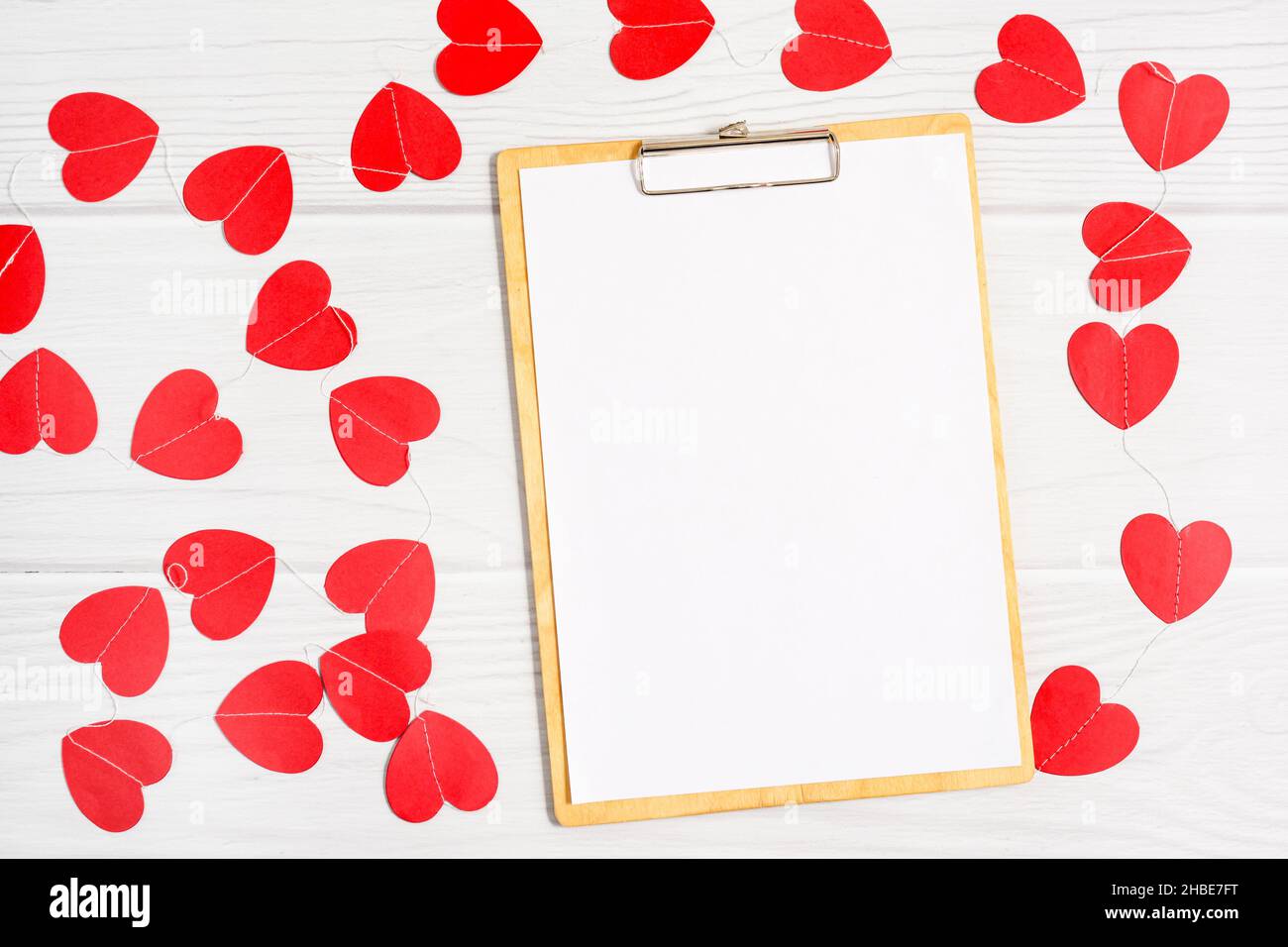 Blank paper on wooden clipboard folder decorated red paper hearts garland Stock Photo