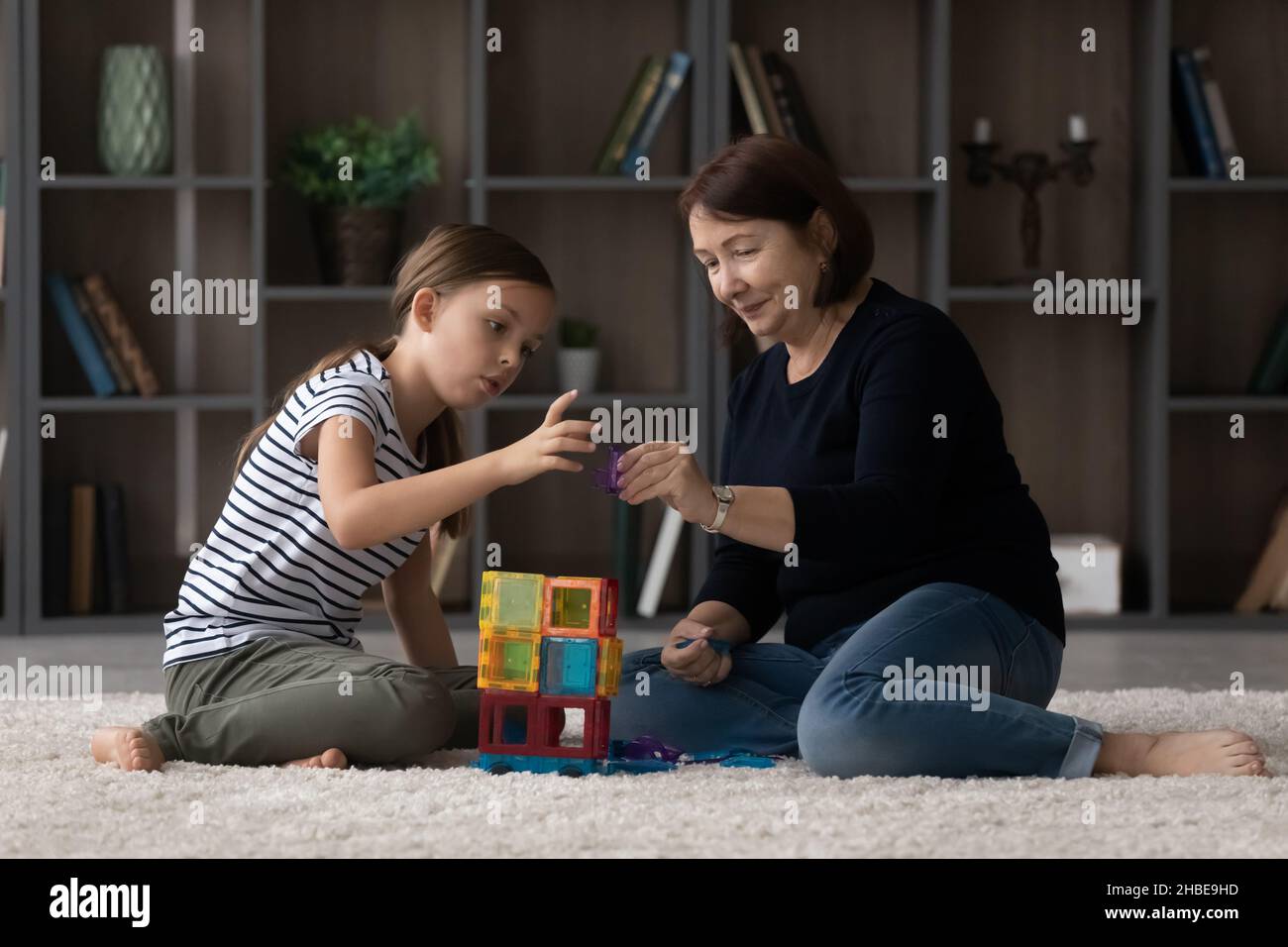 Caring older grandma help granddaughter build from colorful magnetic constructor Stock Photo