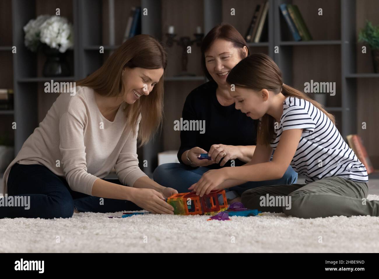 Friendly family of 3 diverse age females playing constructor together Stock Photo