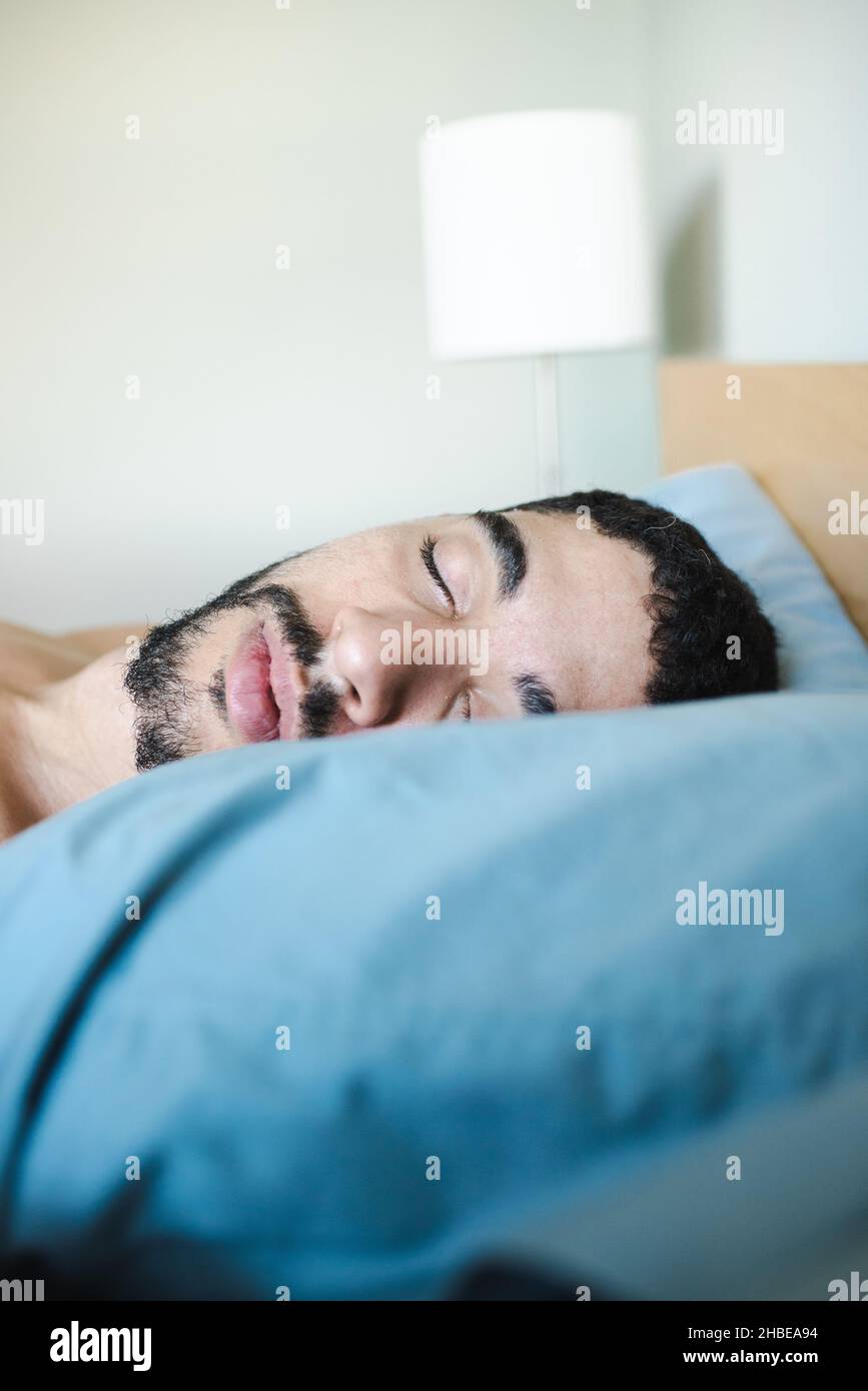 Portrait of a mixed-race bearded millenial half black man sleeping, resting in the morning on a light blue pillow. Young man sleeping peacefully Stock Photo