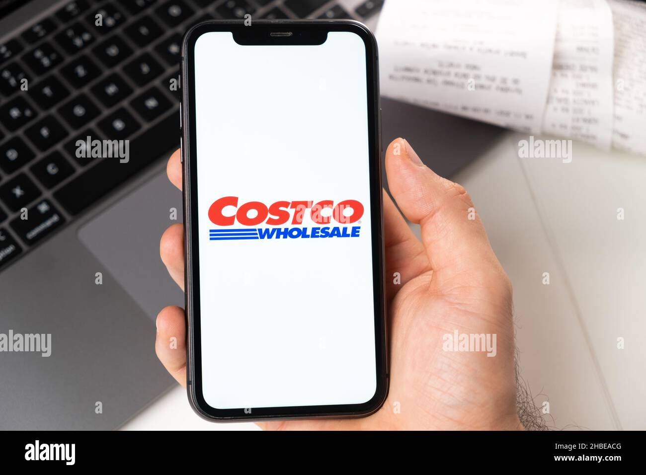 Costco Wholesale application of supermarket and grocery store in a smartphone. A man is holding a smartphone with app for shopping and laptop on the background. November 2021, San Francisco, USA Stock Photo