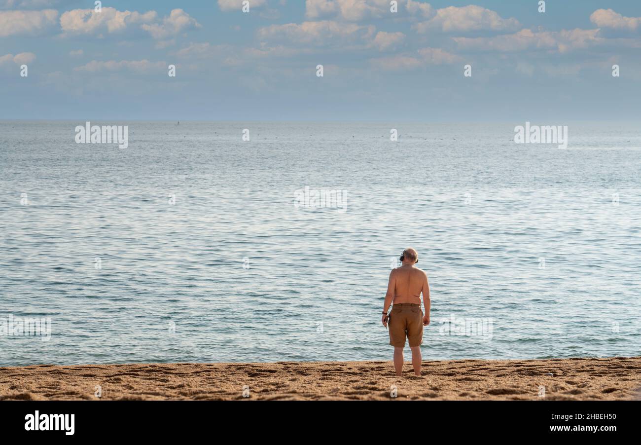 lone mature man stands on beach and looks to sea horizon Stock Photo