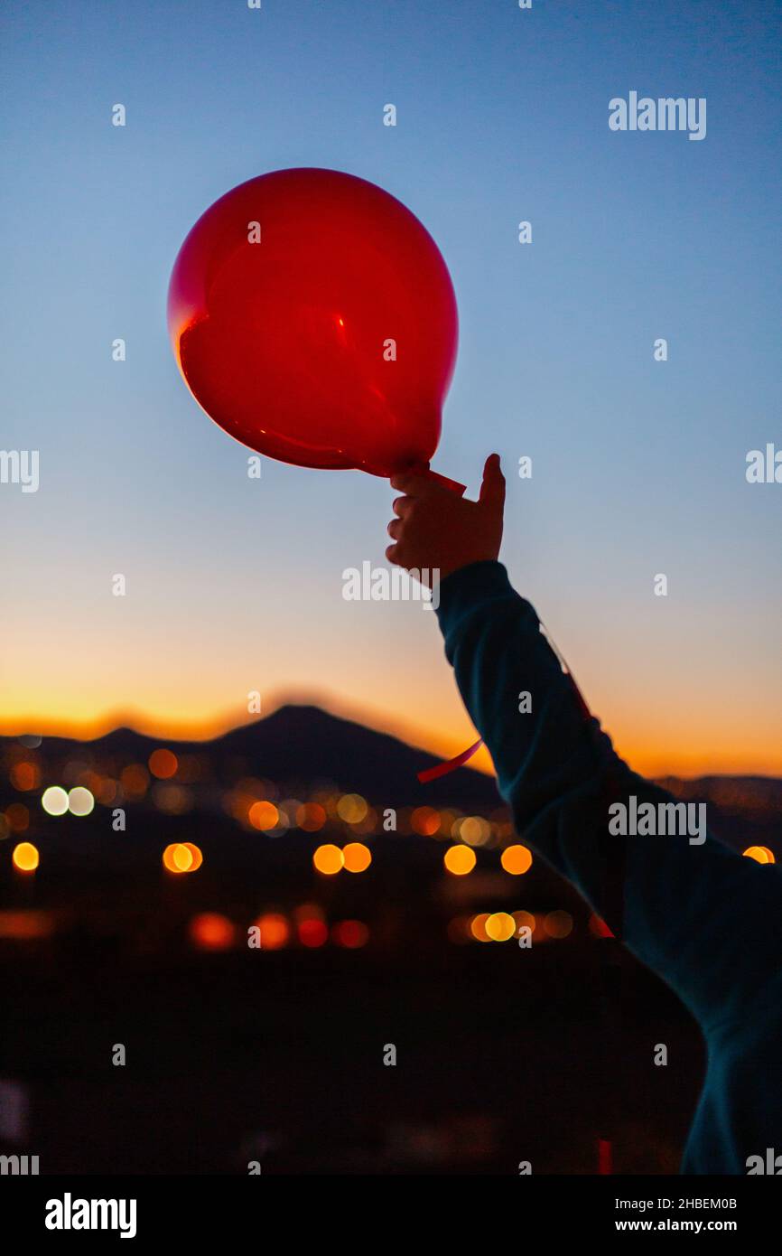 Person releasing a red balloon into the sky at dusk Stock Photo