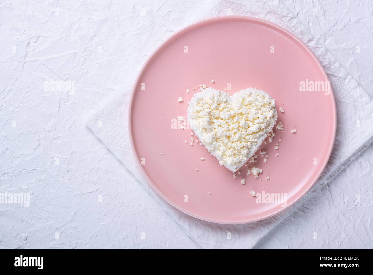 Heart shaped cottage cheese in a pink plate on a white table. Stock Photo