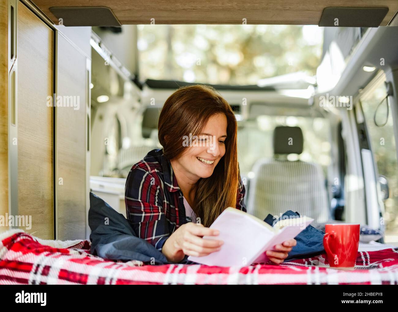 Smiling woman reading book in traveling van Stock Photo