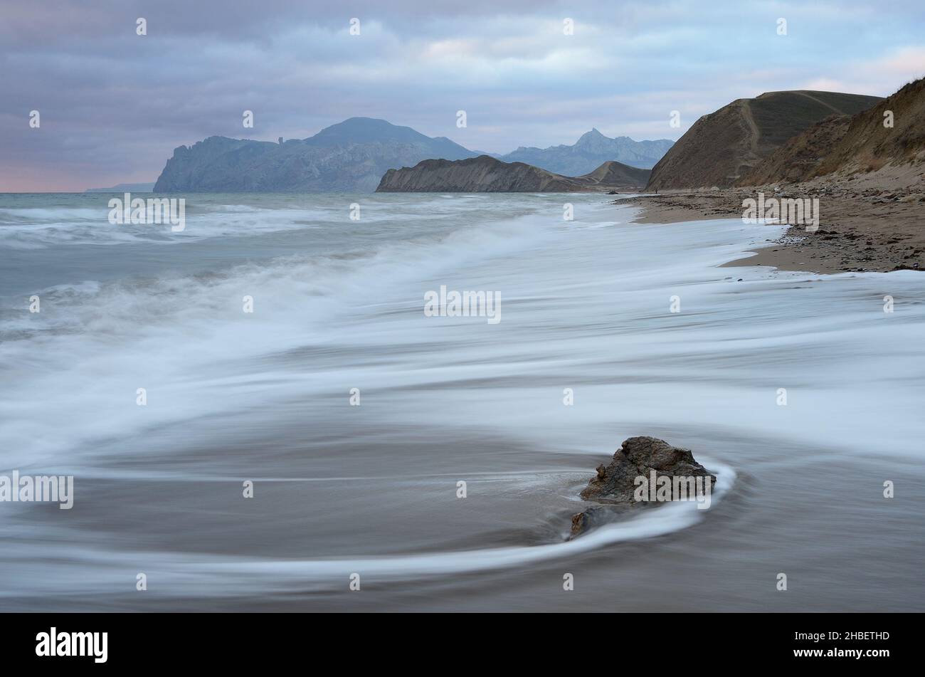Sea landscape with beautiful traces of water on the sand. View of the Cape and the mountain range. Overcast morning with clouds Stock Photo