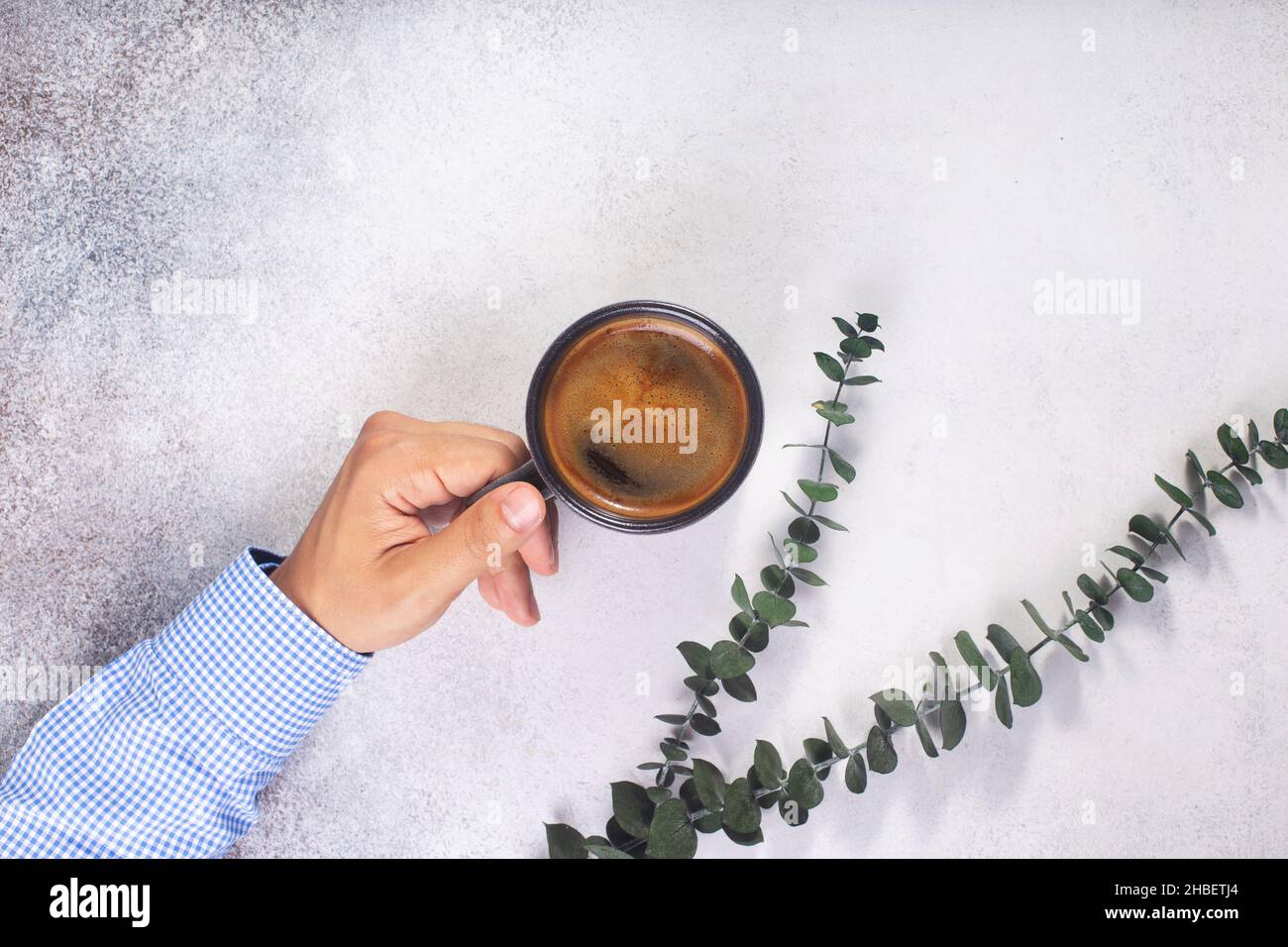 man hand holds a cup of coffee on grey table eucalyptus leaves Stock Photo