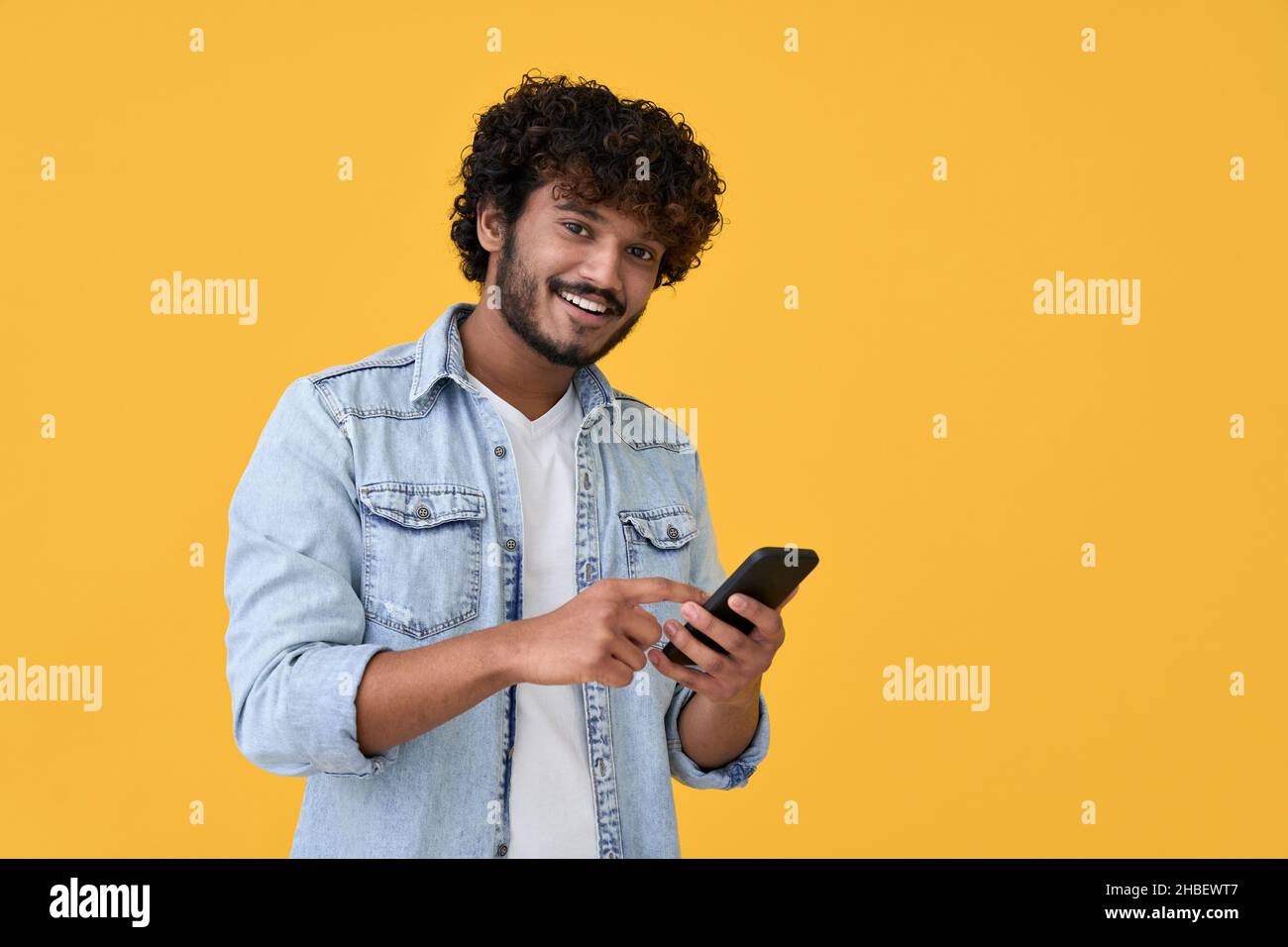 Smiling indian young man using cell phone isolated on yellow background. Stock Photo