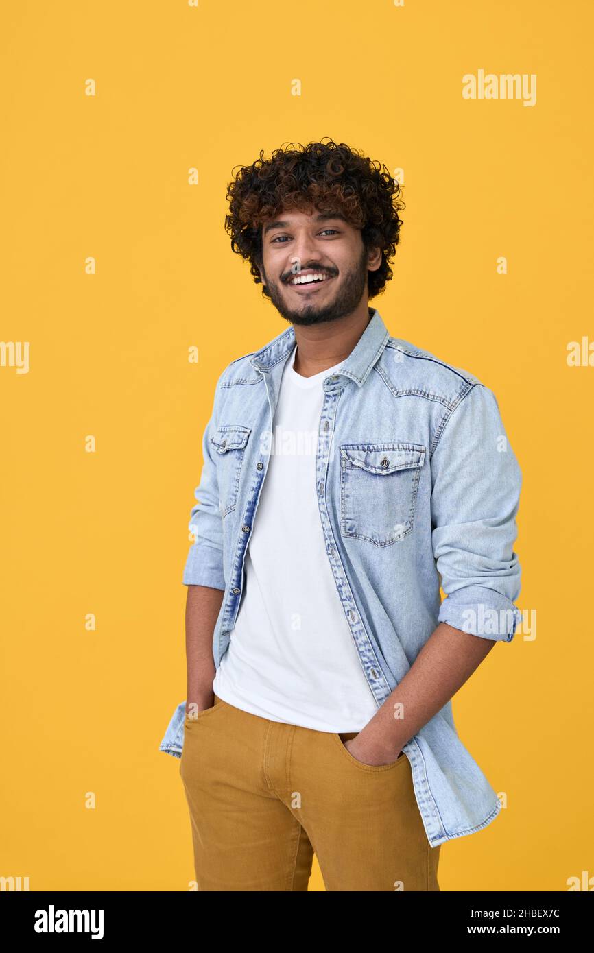 Smiling young indian guy standing isolated on yellow background. Vertical Stock Photo