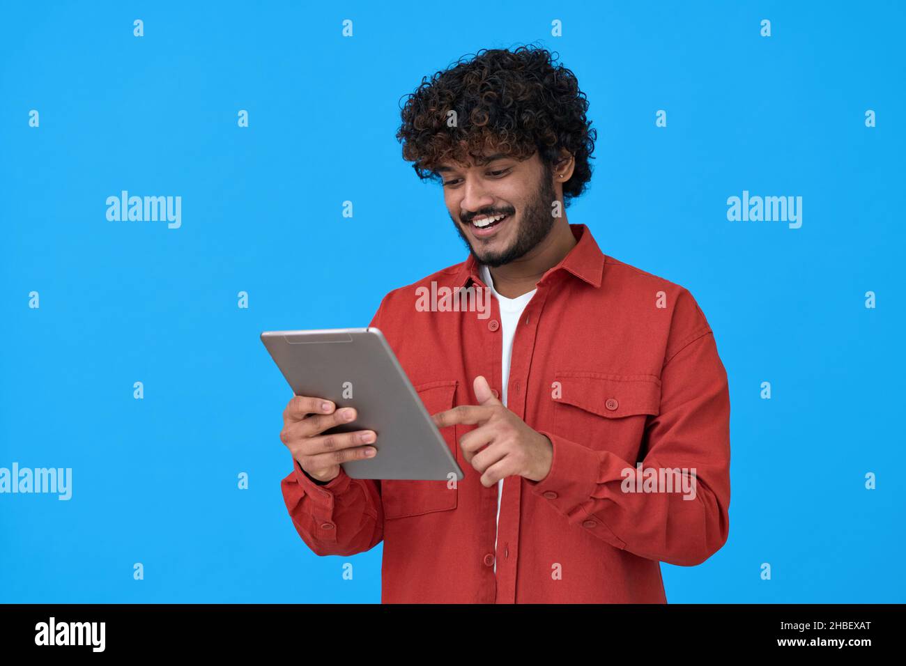 Happy indian guy using digital tablet isolated on blue background. Stock Photo
