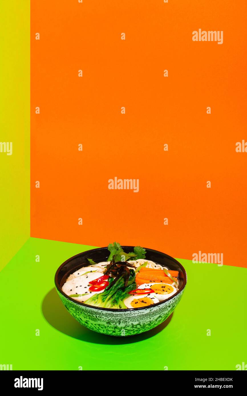 Ramen asian noodle in broth with Beef tongue meat, mushroom and pickled egg in bowl on green and orange background Stock Photo