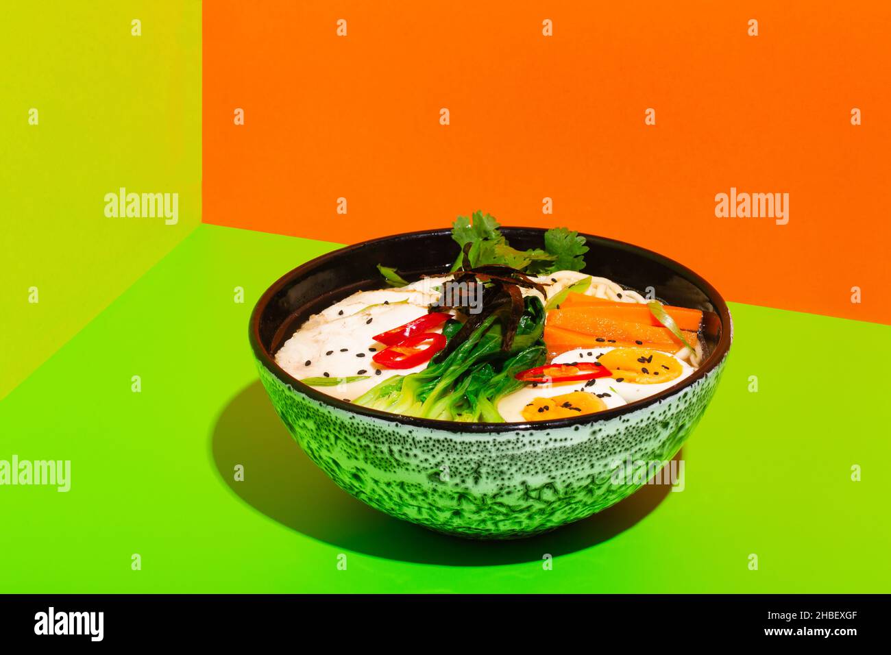 Ramen asian noodle in broth with Beef tongue meat, mushroom and pickled egg in bowl on green and orange background Stock Photo