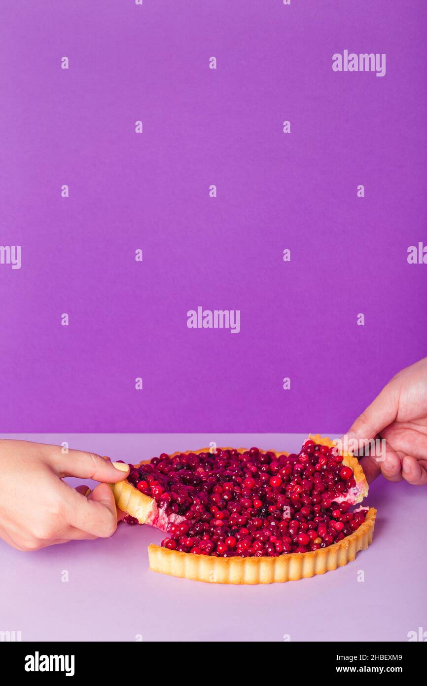 Hand takes cranberry Tart.Delicious cranberry tart with jellied and fresh cranberries for Christmas on violet background Stock Photo