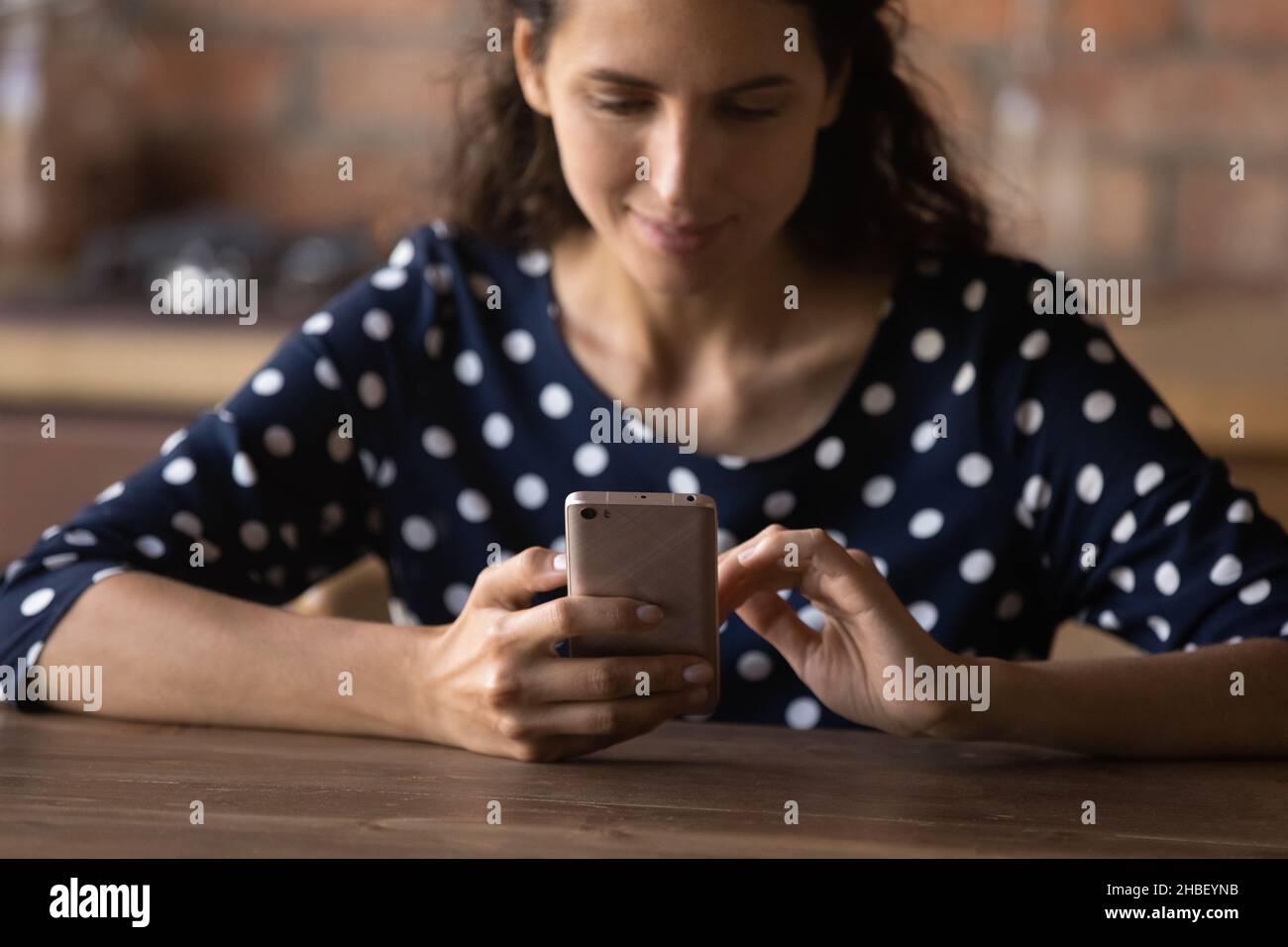 Smiling latin woman using smartphone, sitting at table. Stock Photo