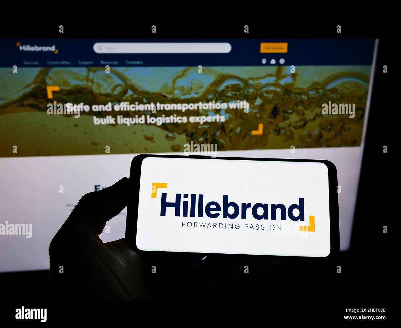 Person holding cellphone with logo of German logistics company  J.F. Hillebrand Group AG on screen in front of webpage. Focus on phone display. Stock Photo