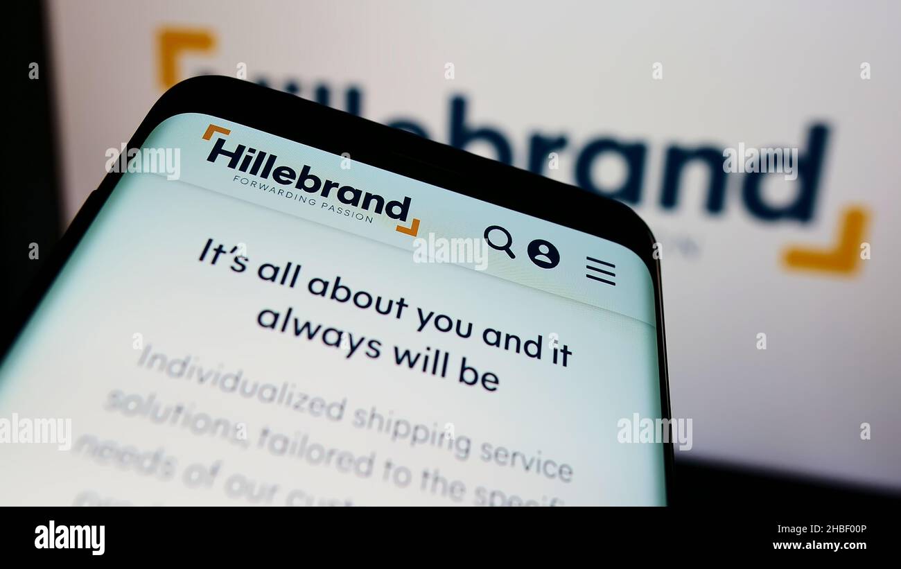 Mobile phone with website of German logistics company  J.F. Hillebrand Group AG on screen in front of logo. Focus on top-left of phone display. Stock Photo